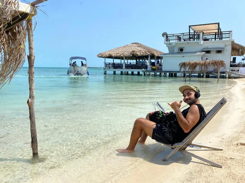 Mike wearing headphones and carrying his sound kit on a chair beside the water in Belize