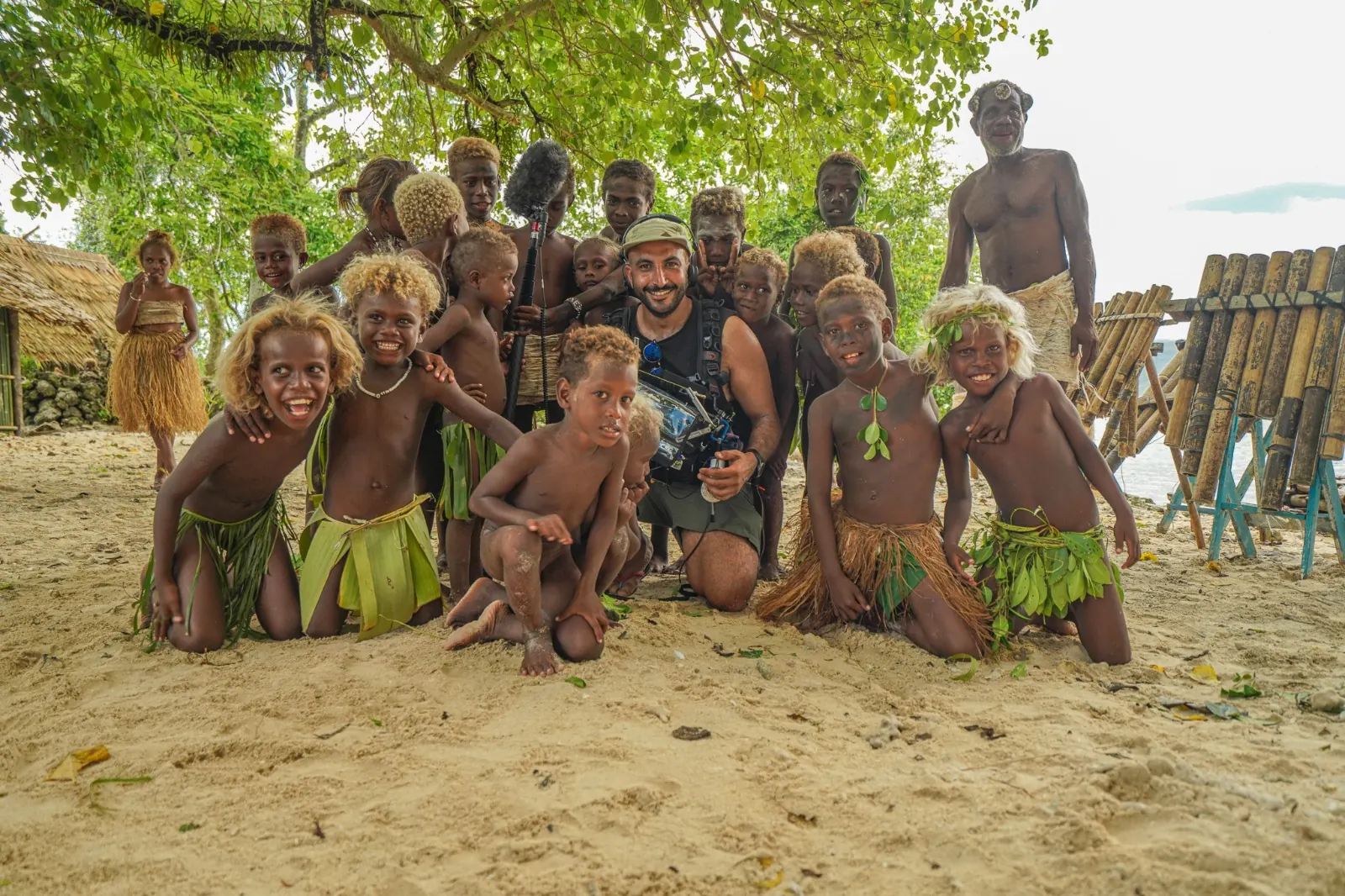 Mike with his recording equipment posing with a group beneath trees in the Solomon Islands