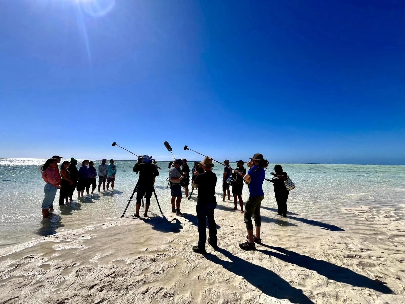 Camera and sound crew filming a group in shallow water on a sandbank